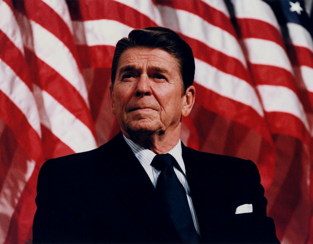 Ronald Reagan giving a speech in front of American flags.