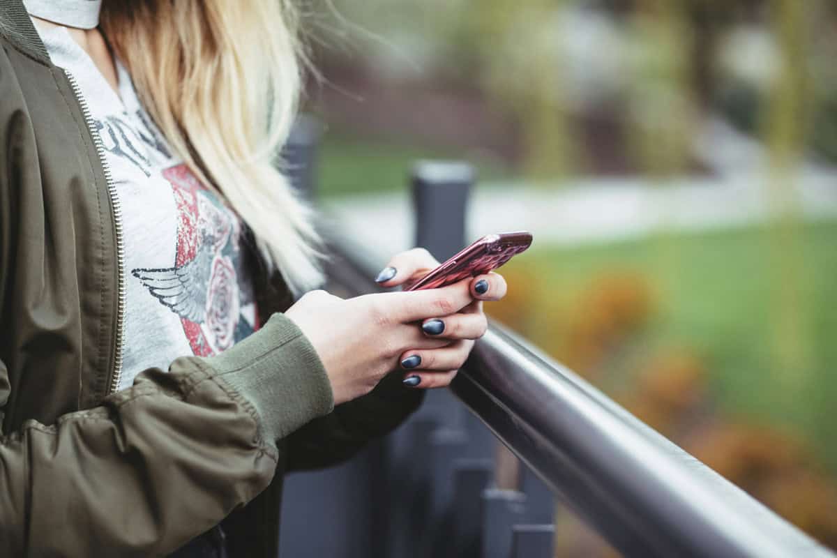 I woman stands outside holding her phone.