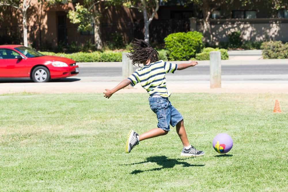 A boy kicking a ball as seen from the back.