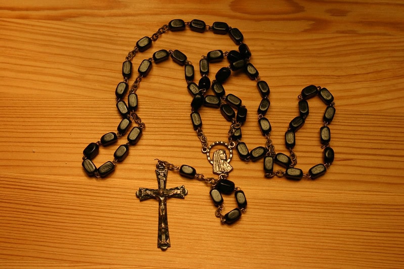 A dark brown rosary on a medium brown wooden table.