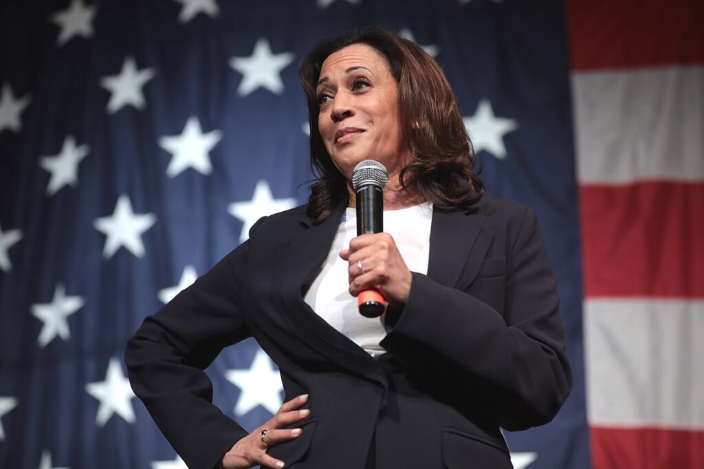 VP Kamala Harris standing with hand on hip and microphone in the other hand.