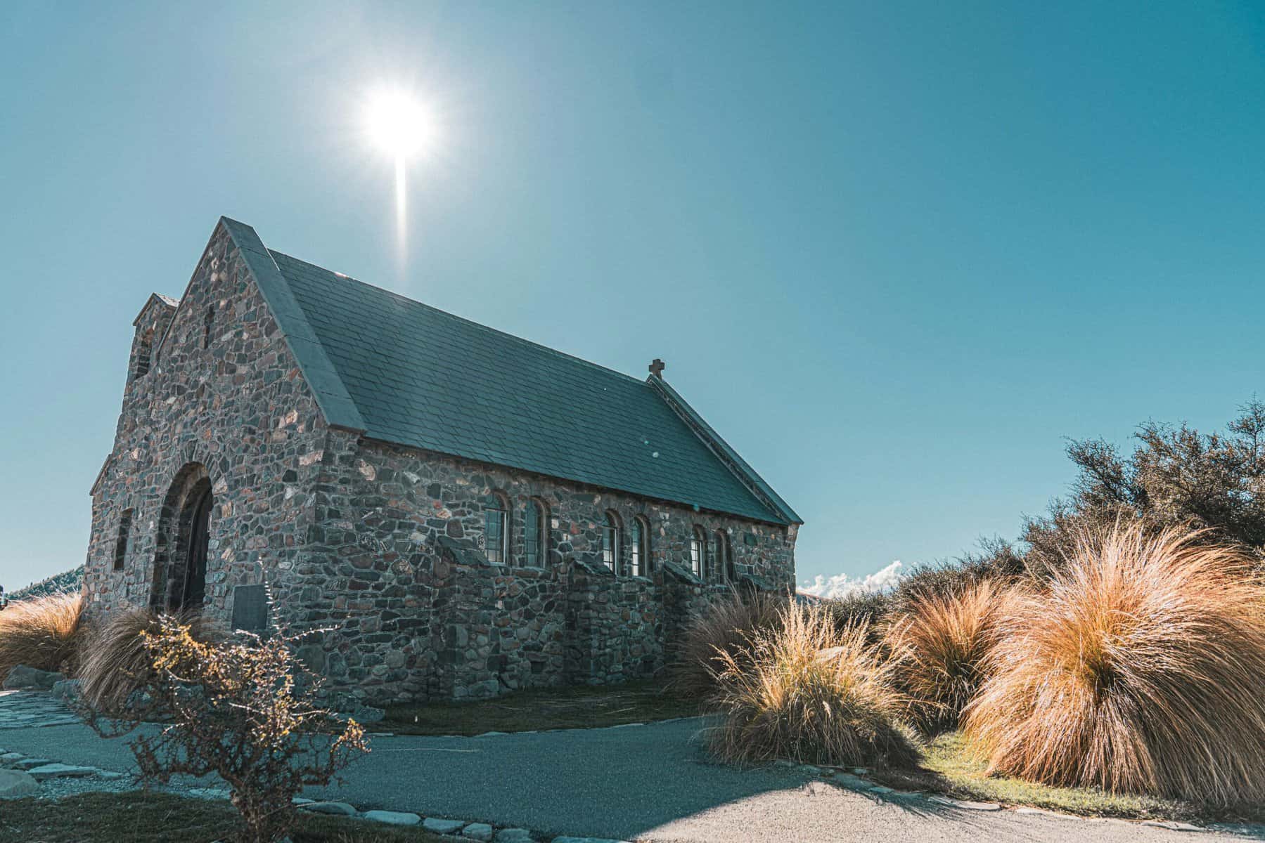 A stone church is seen with the sun behind it.