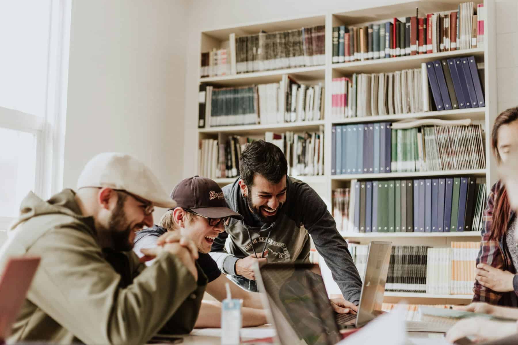 Three men in a library looking at a laptop and laughing.