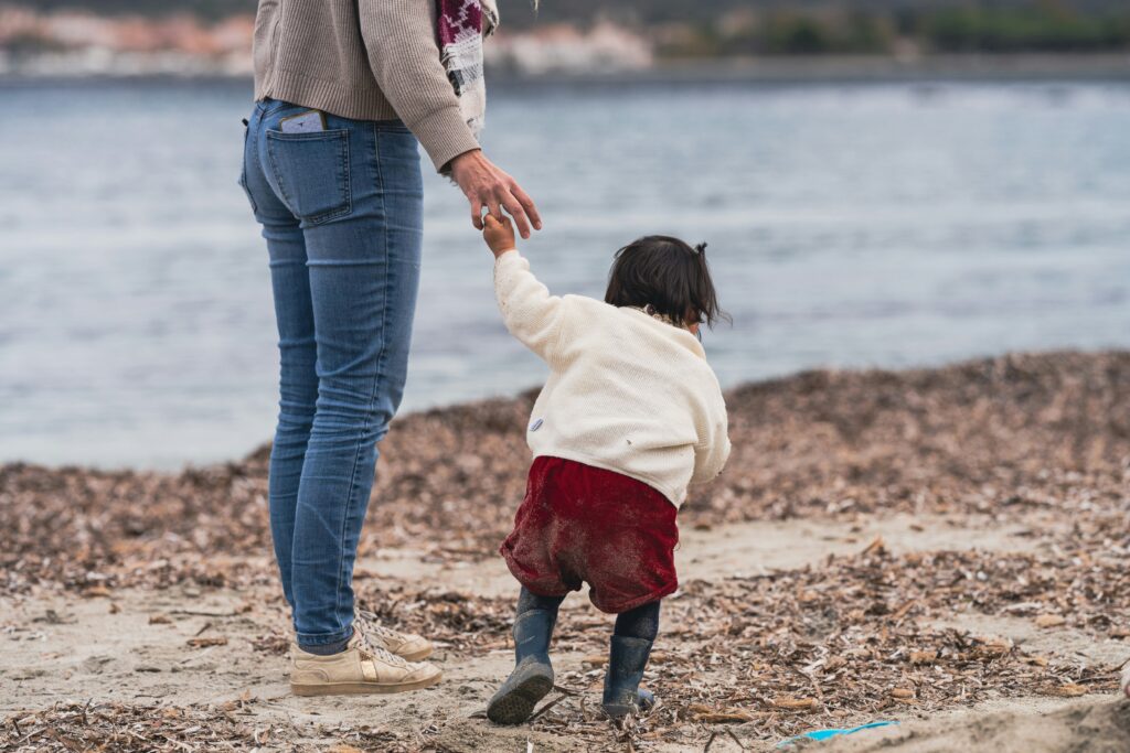 Woman holding a toddler's hand on the beach.