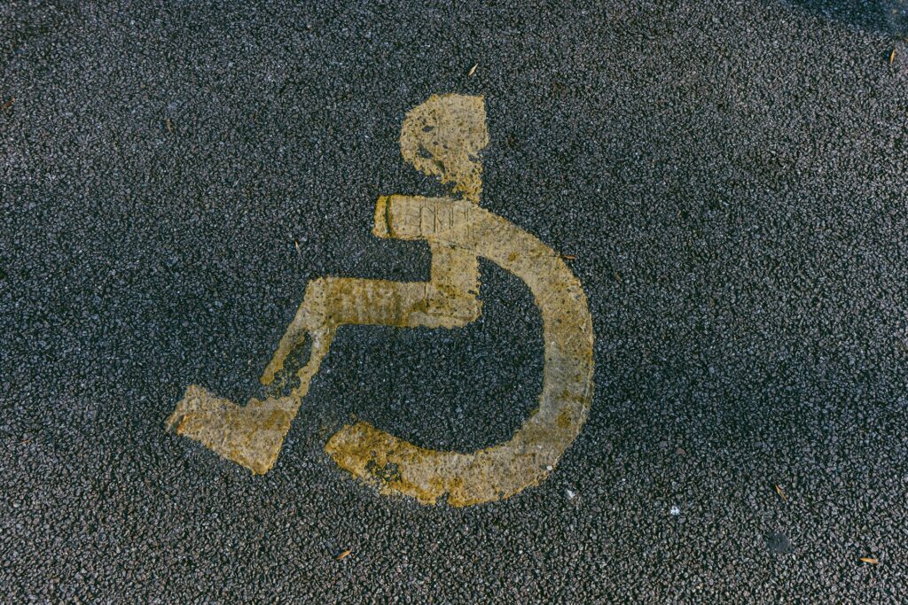 Worn yellow handicap symbol painted on asphalt.