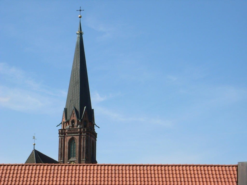 An old church steeple seen over a red tile roof.