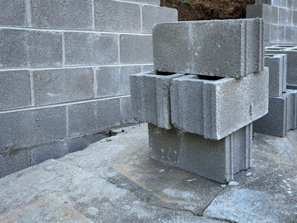 Four grey cinder blocks, stacked in front of a cinder block wall.