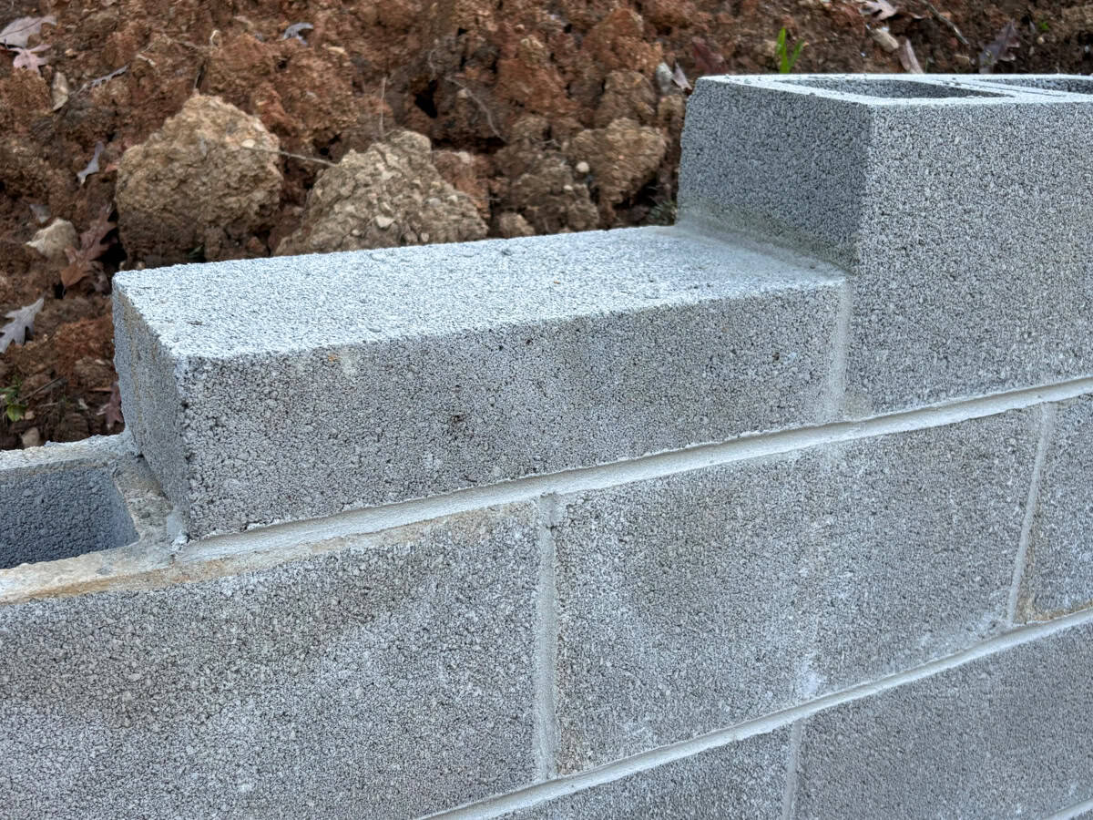 The top of a partially complete grey cinder block wall with dirt piled behind it.