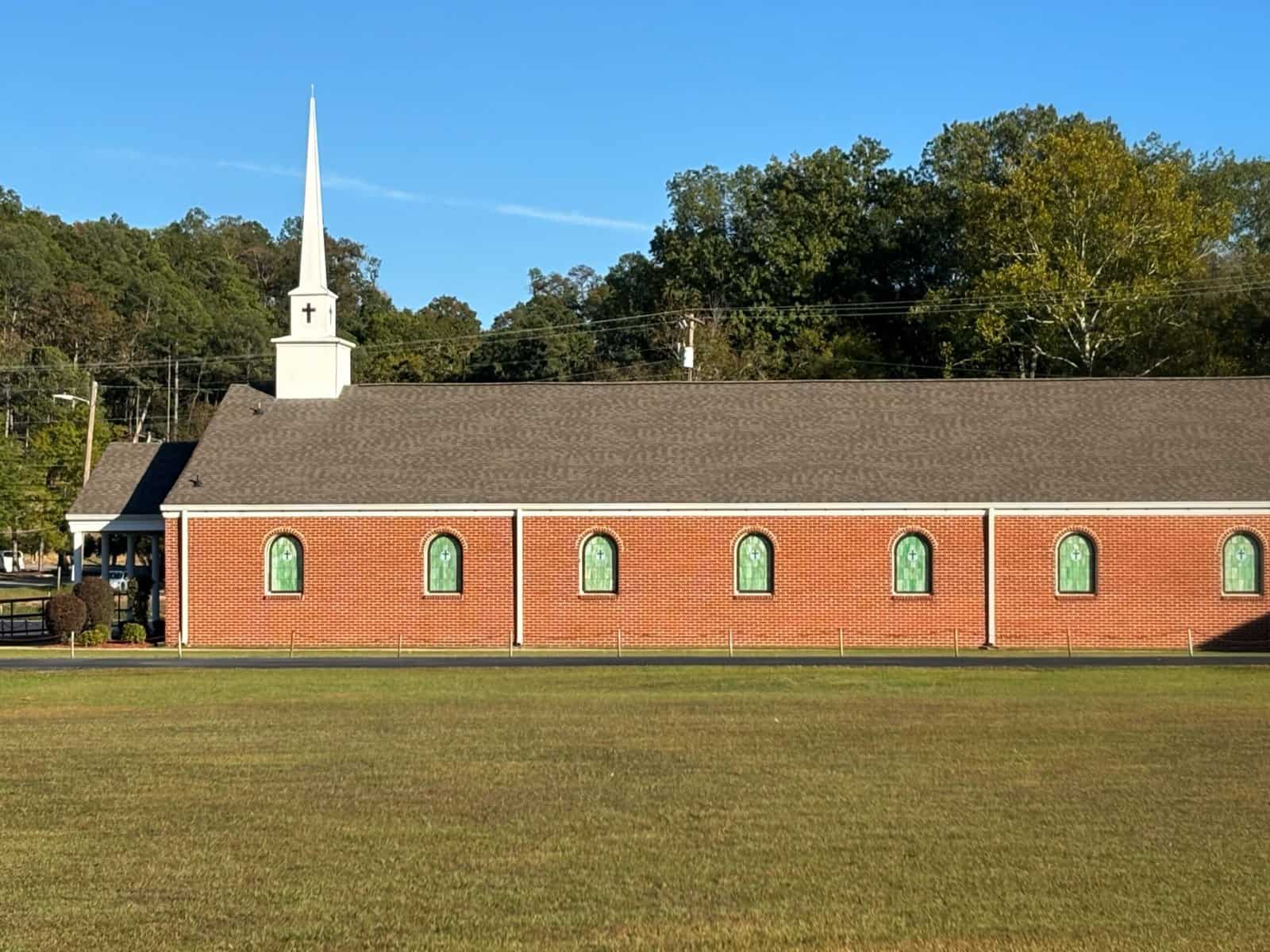 Side view of a one story red brick church with a white steeple.