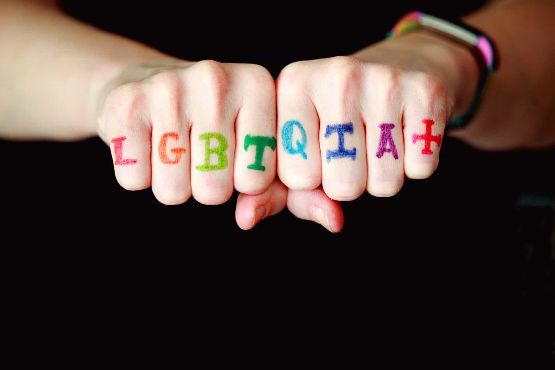 LGBTQIAH+ Written across someone's fingers.