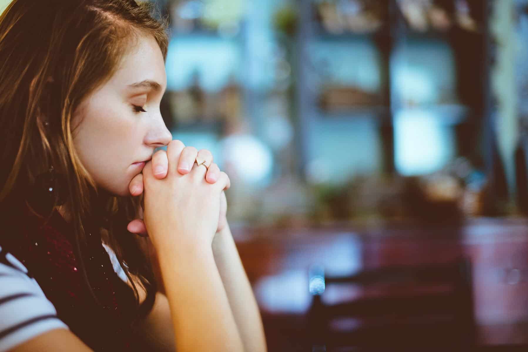 A woman has her hands folded in prayer.