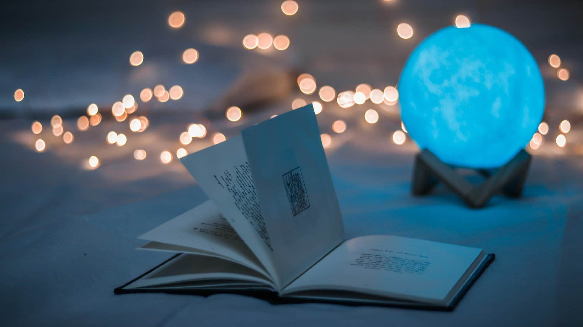 A magical looking scene with a book, fairy lights, and an illuminated ball.