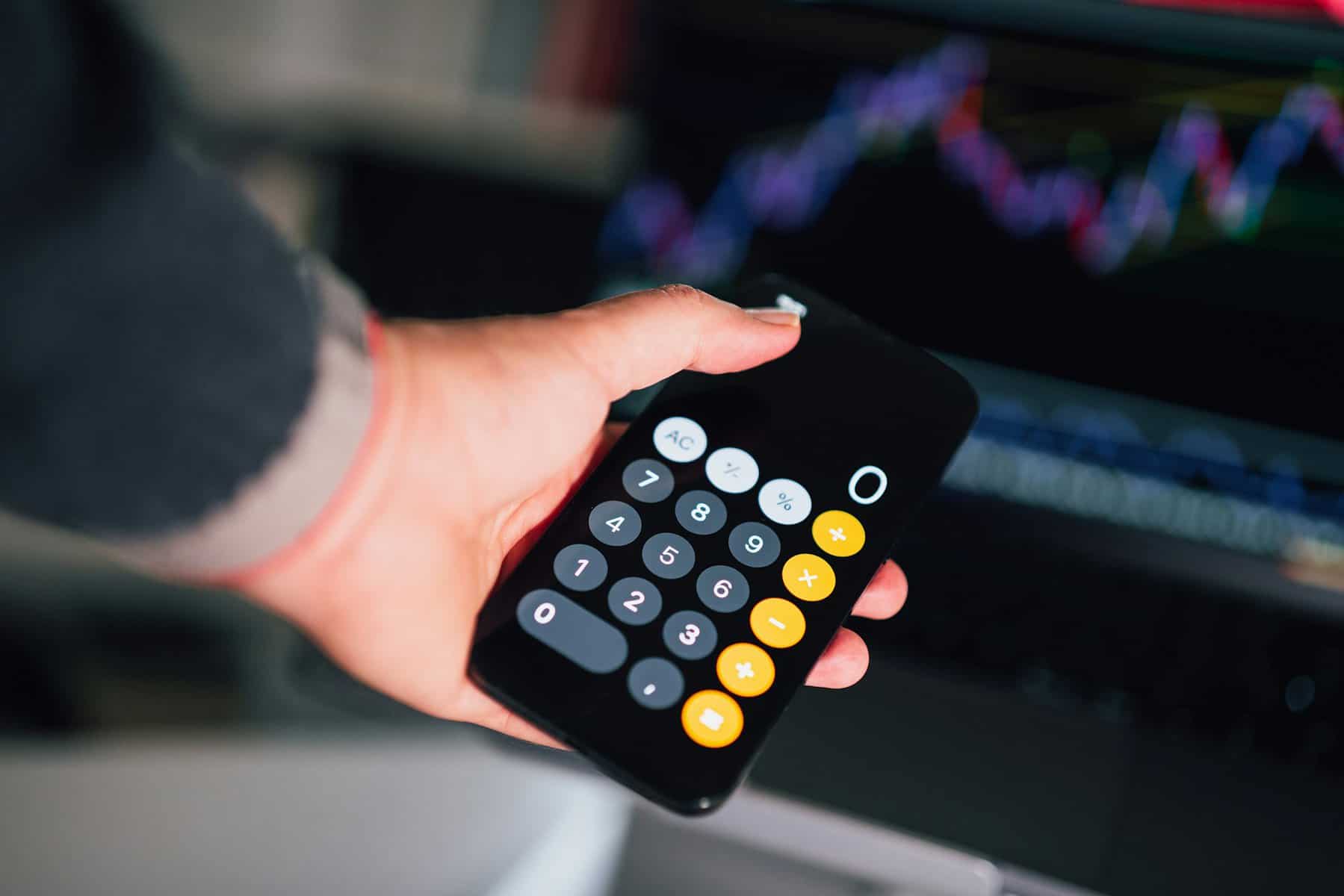 A person holds a calculator set at zero with an out of focus graph in the background.