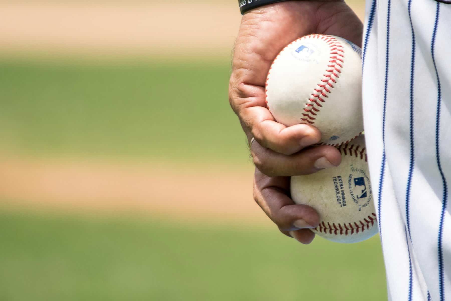 A man's hand is shown closeup against his uniformed leg holding two baseballs at his side.