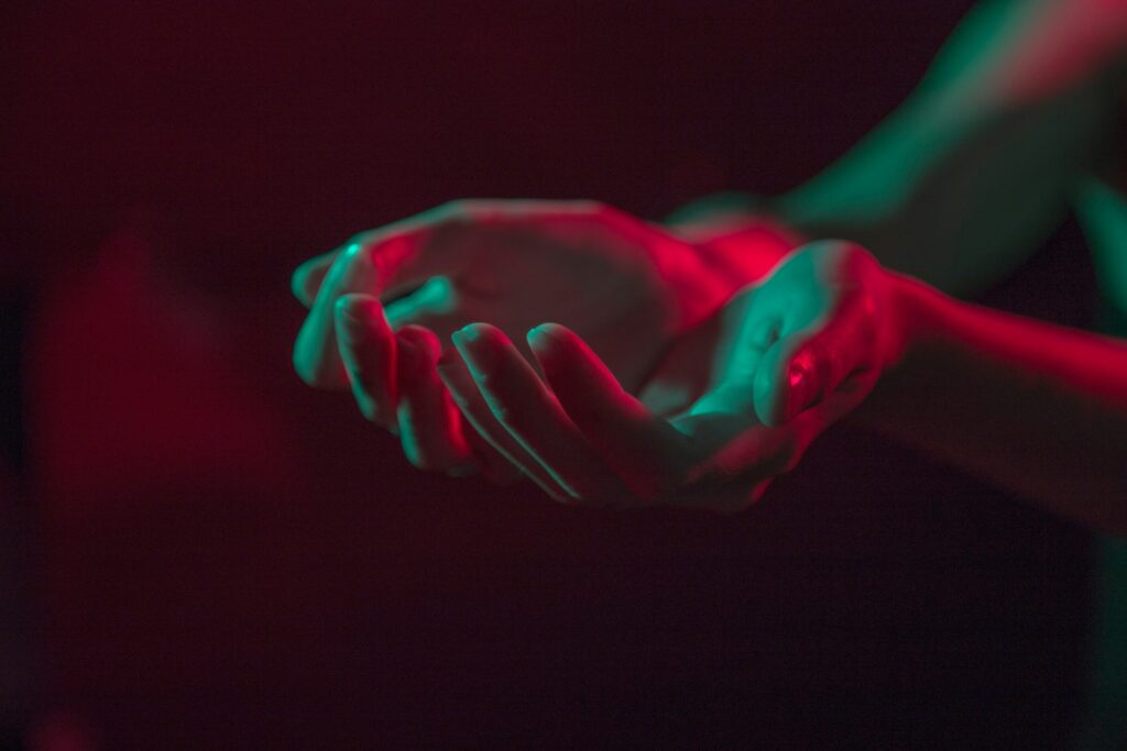 Two hands help out in a cupped position and lit by red and green light.