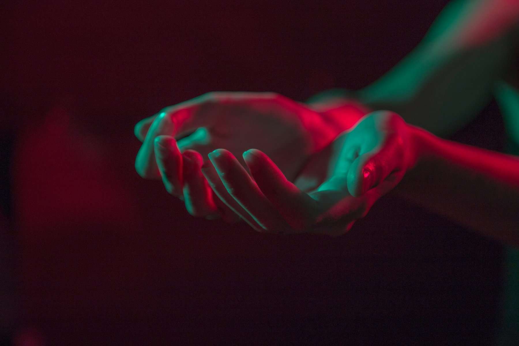 Two hands help out in a cupped position and lit by red and green light.