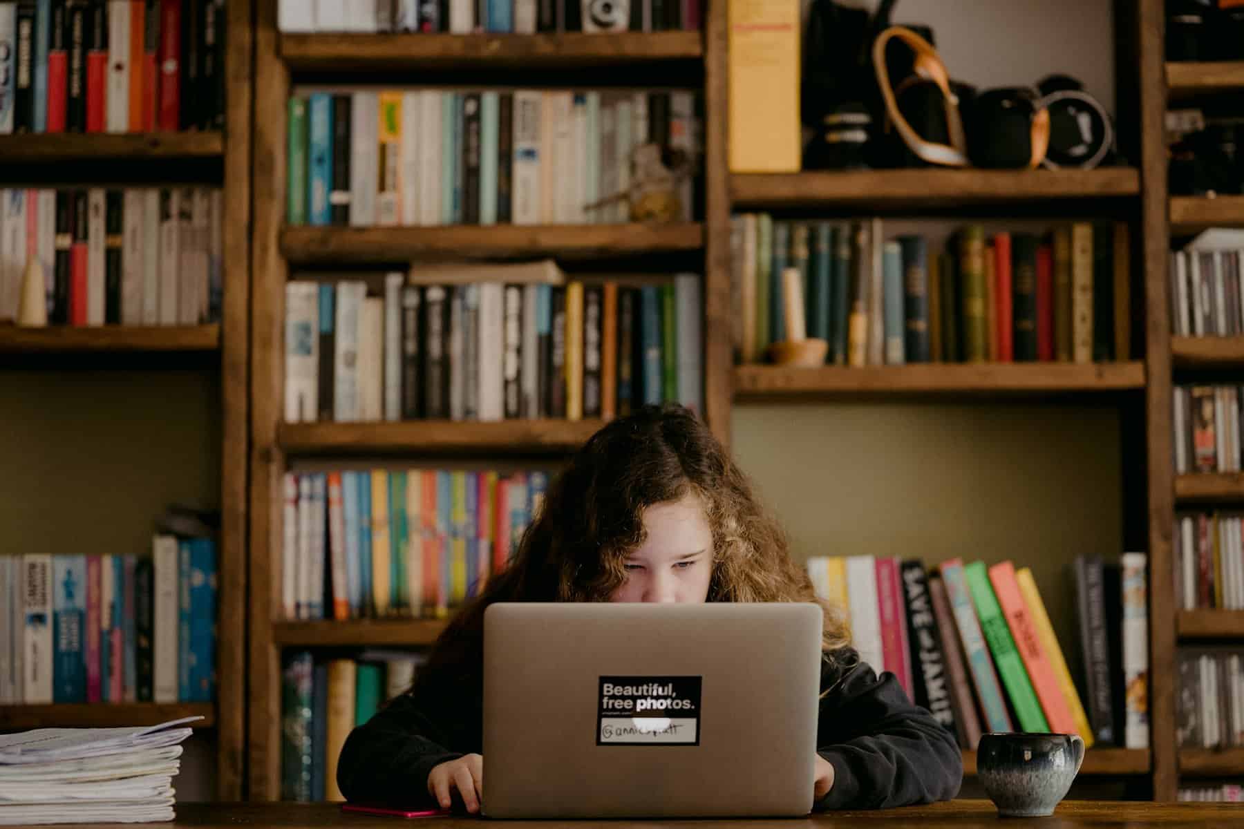 A girl sits behind and is half obscured by a desk and laptop.