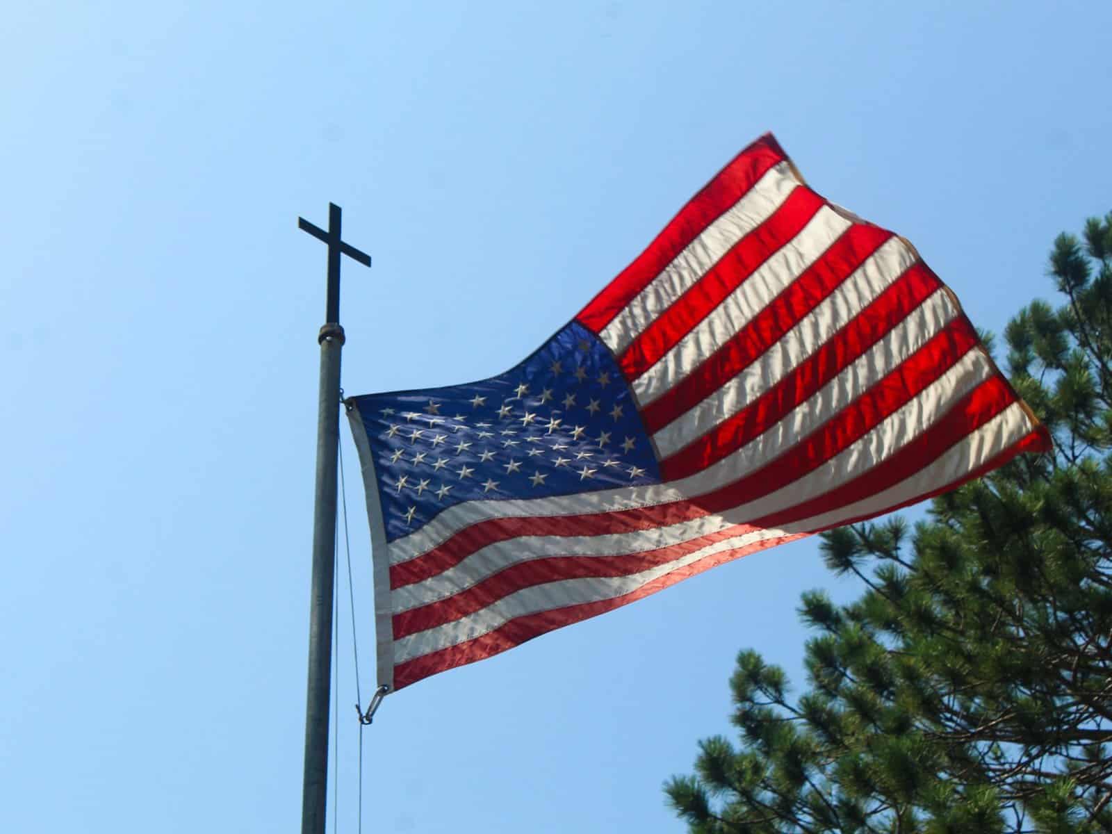 An American flag hangs on a flagpole with a cross on top of it.