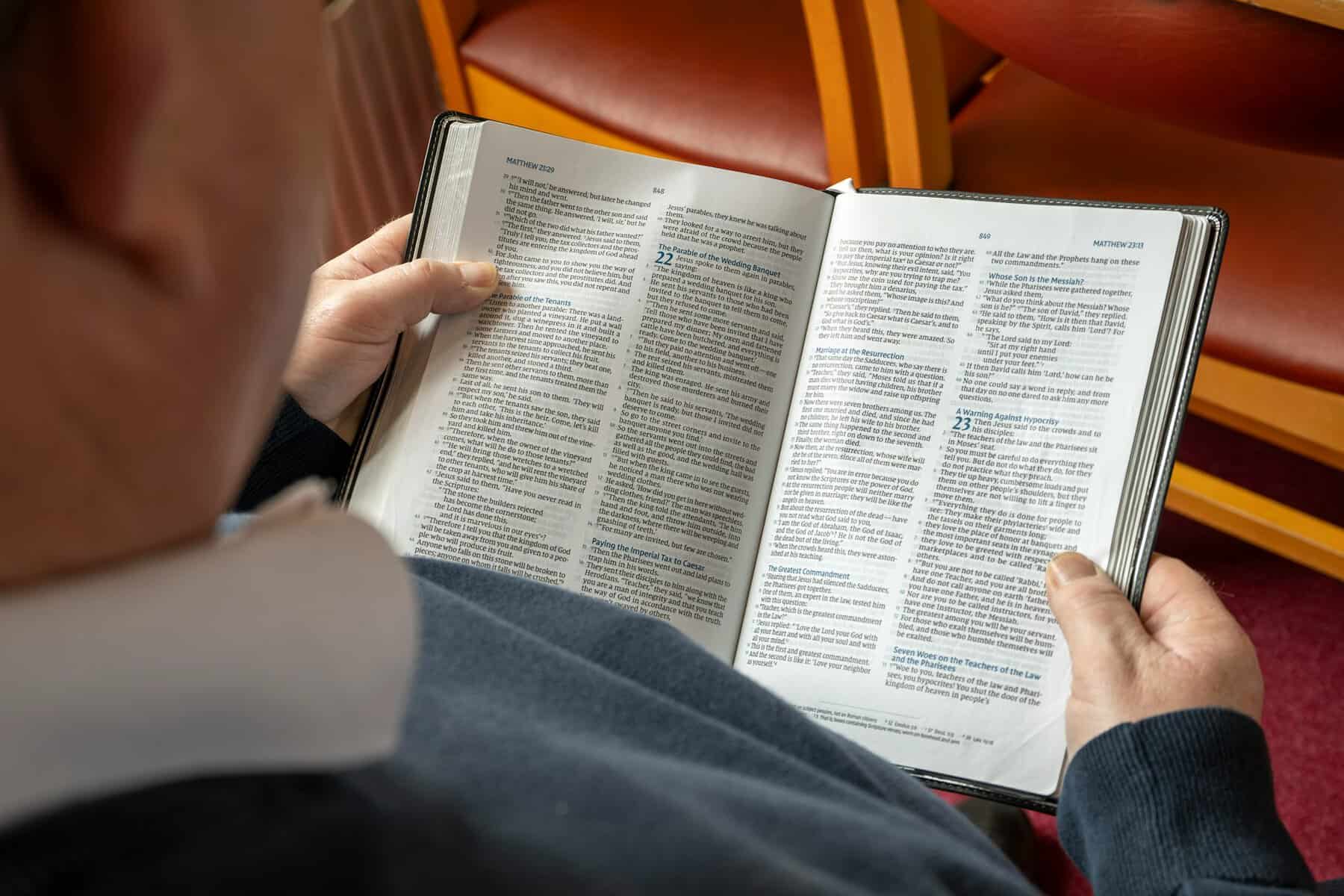 An older person holding a Bible open to the book of Matthew.