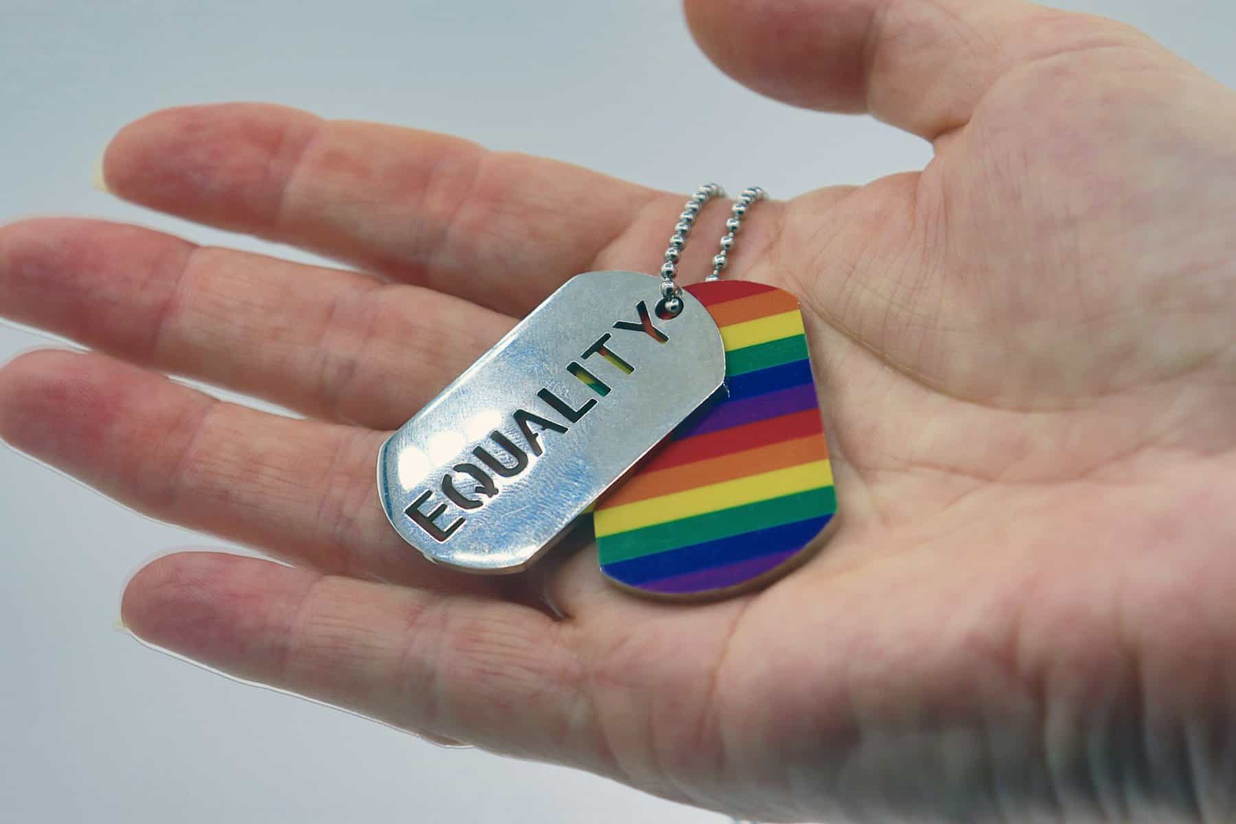 An open hand holds dog tags- one a rainbow, the other say' equality.