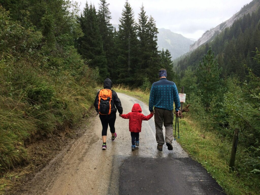 Two adults and a child walk away from a camera on a wet day on an apparent hike.