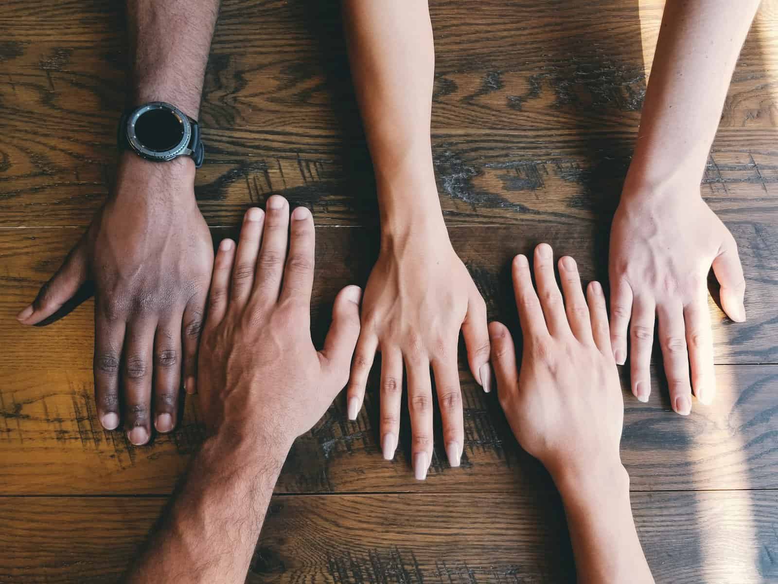 Five hands from men and woman shown flat on a table.