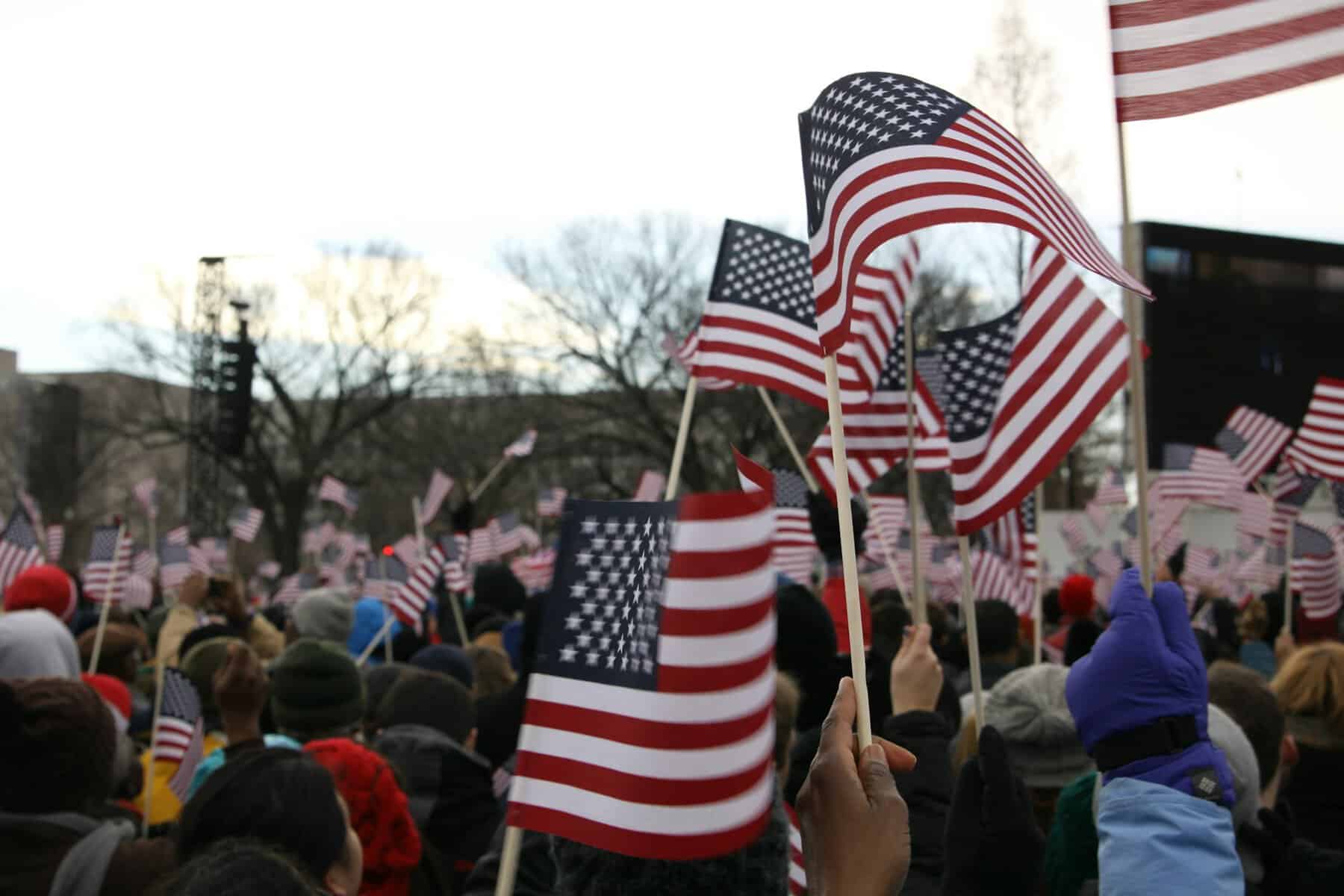 A crowd of people wave small American flags, seen close up.