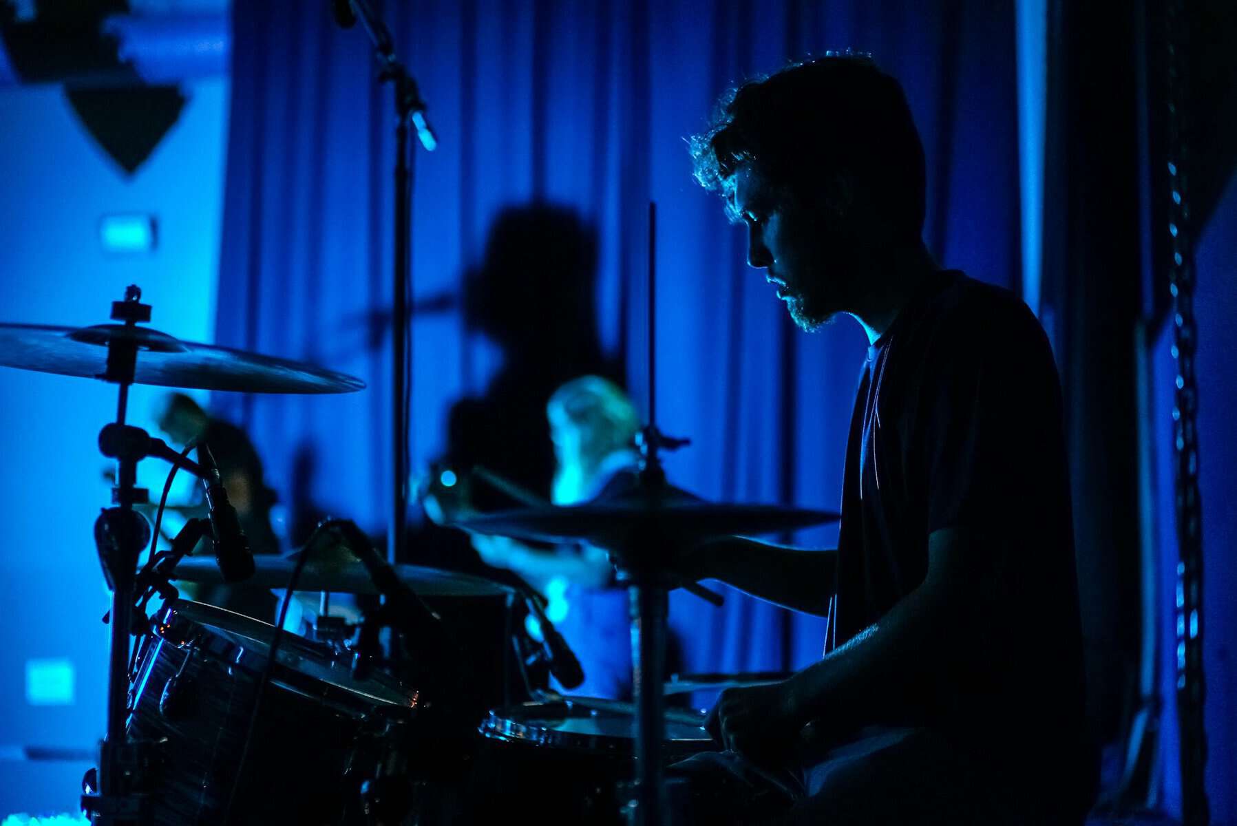 A man sits at a drum set in very low light.