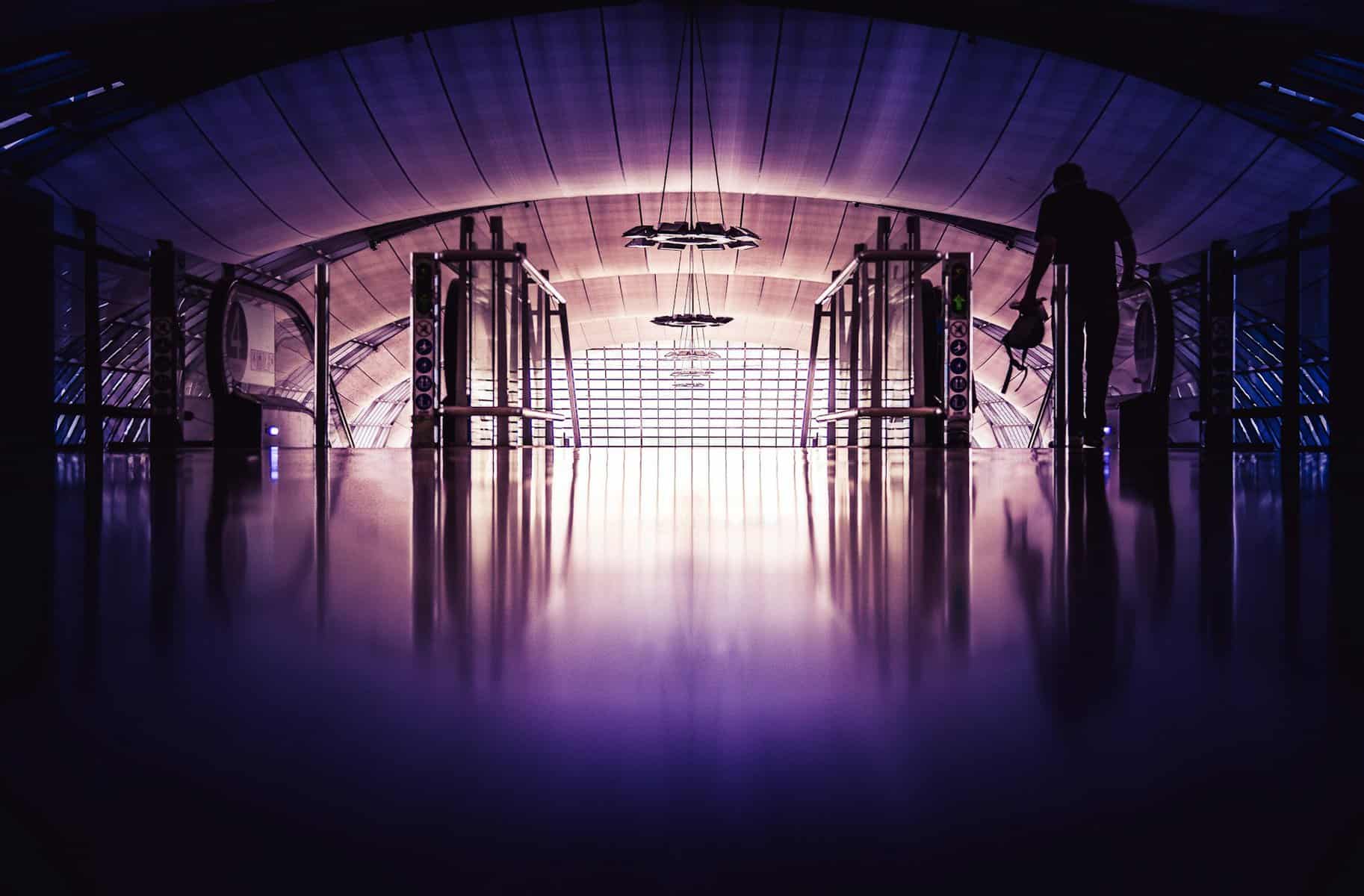 Moody photo of a man in an airport about to go down an escalator.