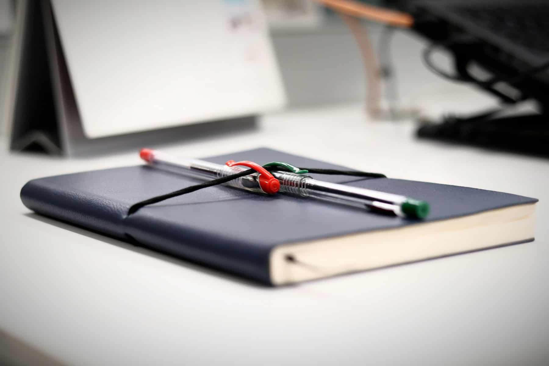 A black notebook with a red and black pen on top.