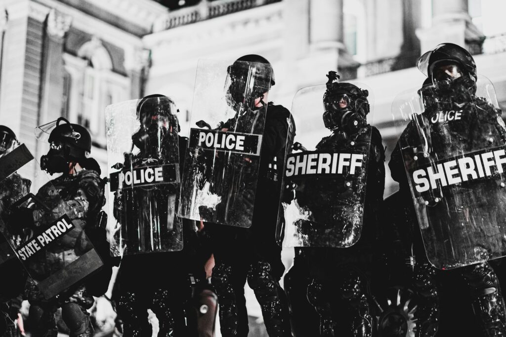 Law enforcement from various agencies stand guarded by shields.