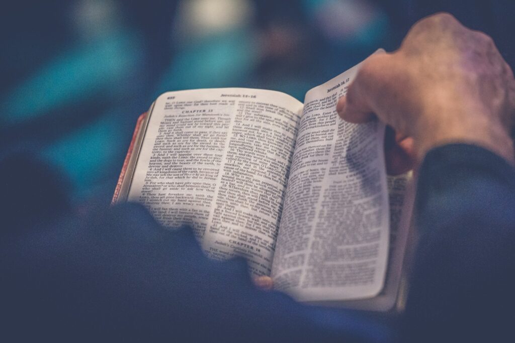 An open Bible sits on a man's lap as he begins to turn a page.