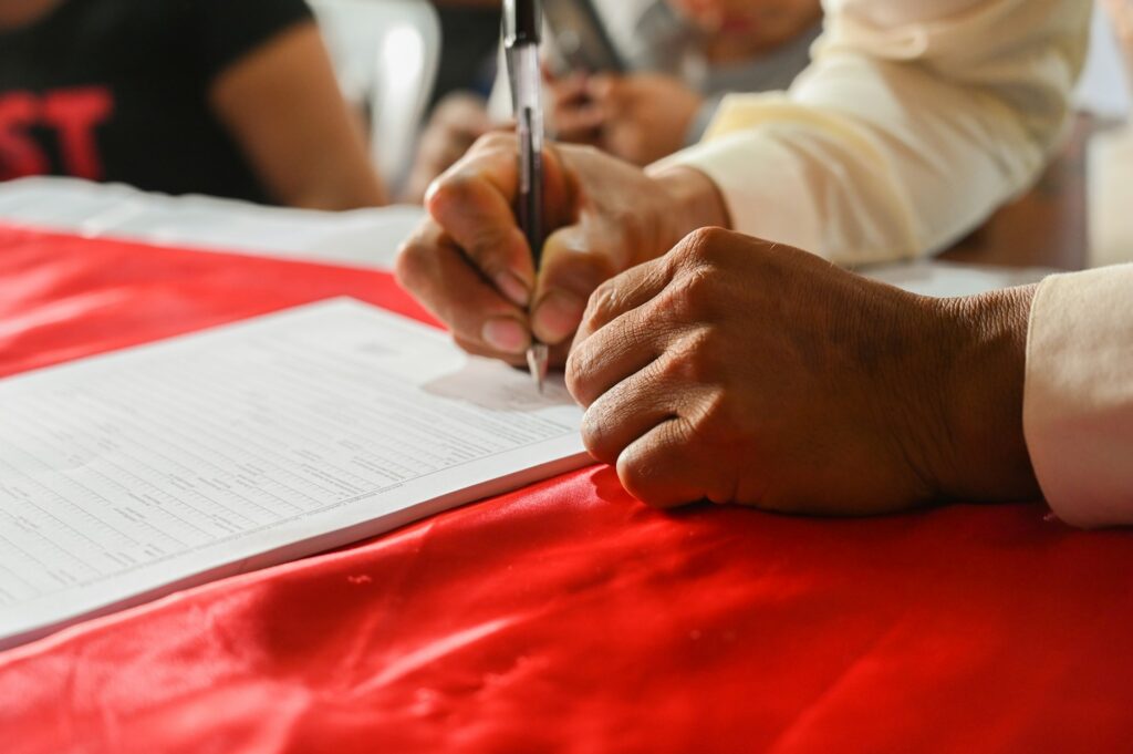 Hands of an older man signing a piece of paper.