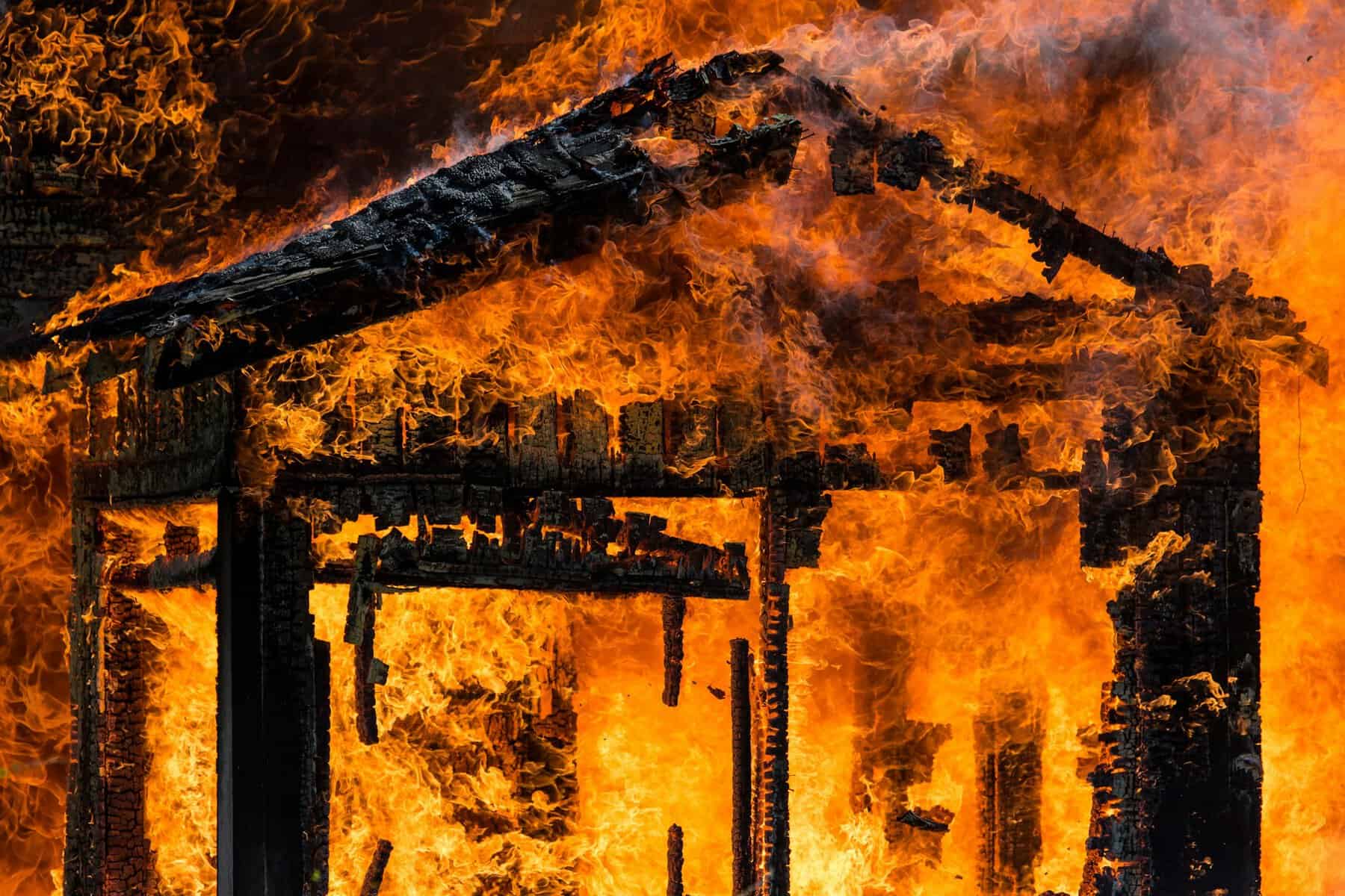 A building engulfed in flames with deeply charred support beams visible.