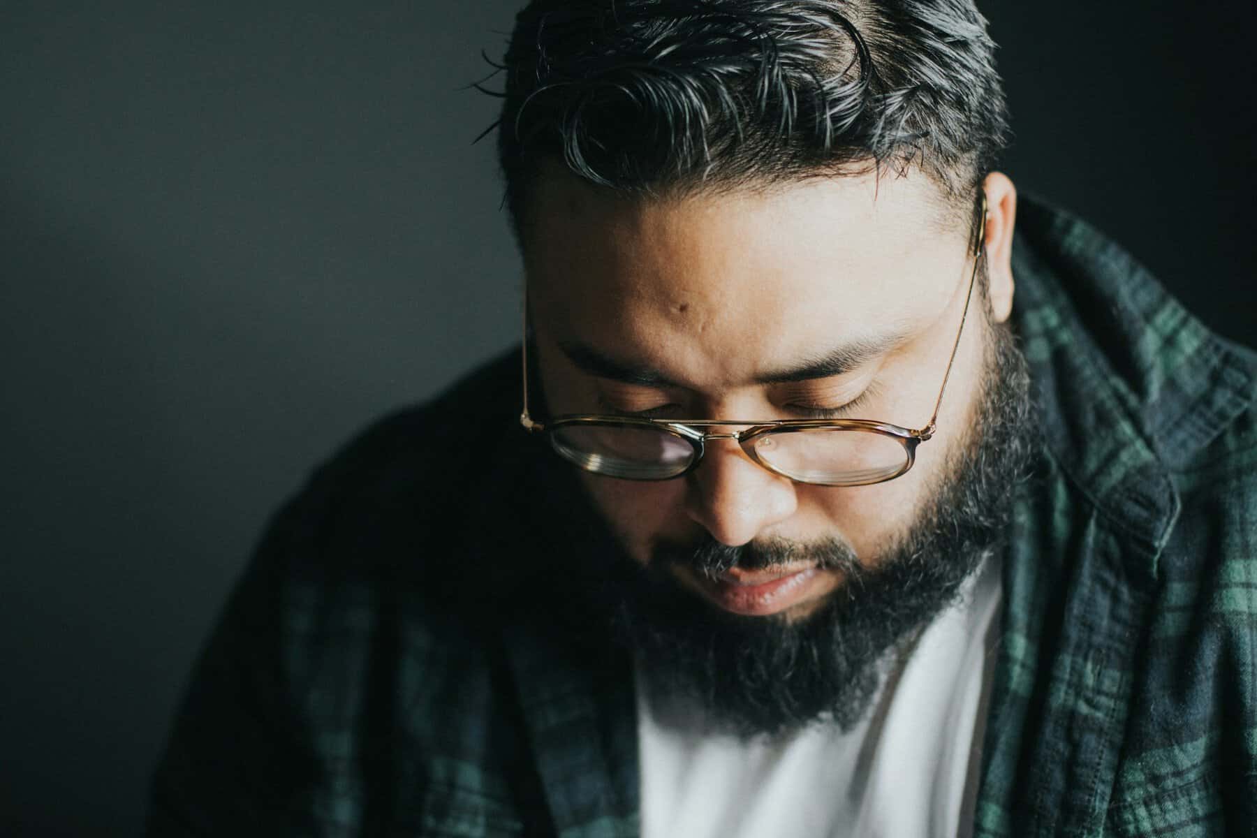 A Latino looking man wearing glasses has his head bowed.