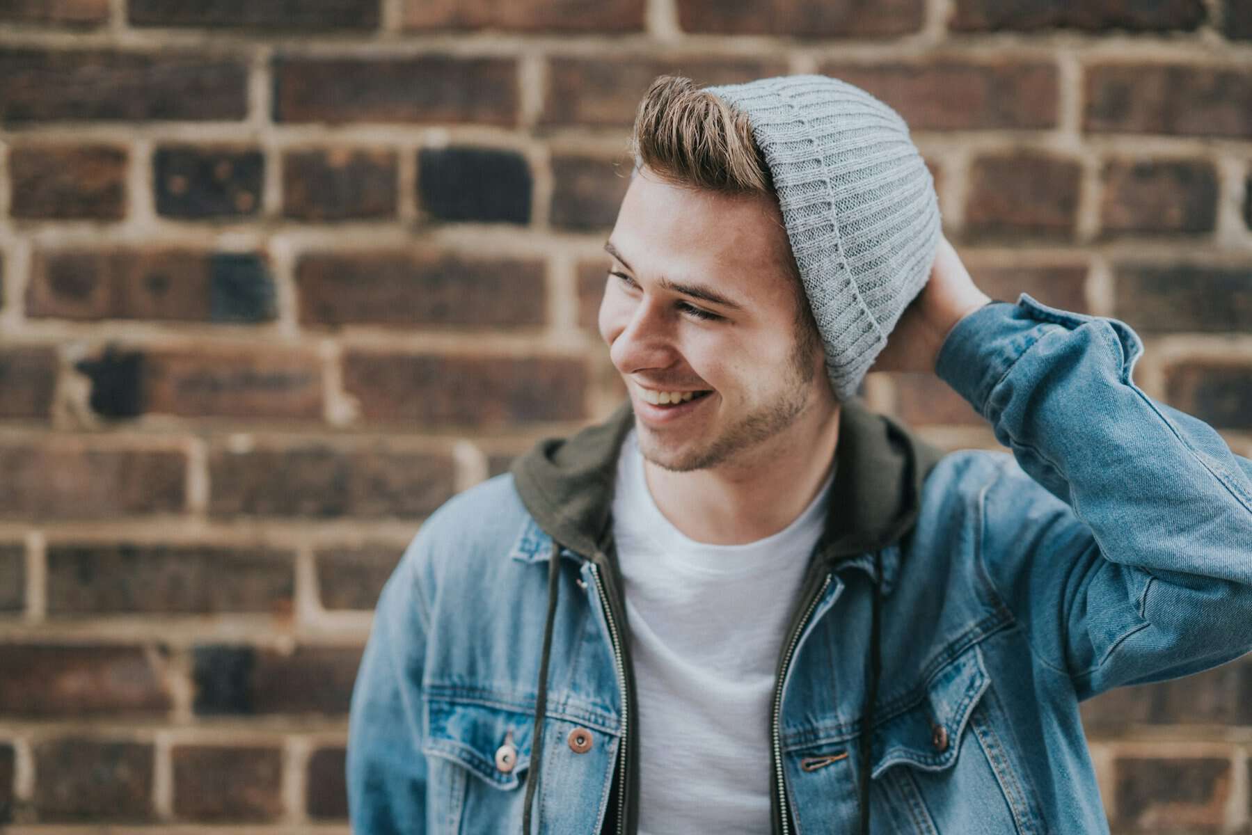 A young man wearing a beanie hat in front of a brick wall.