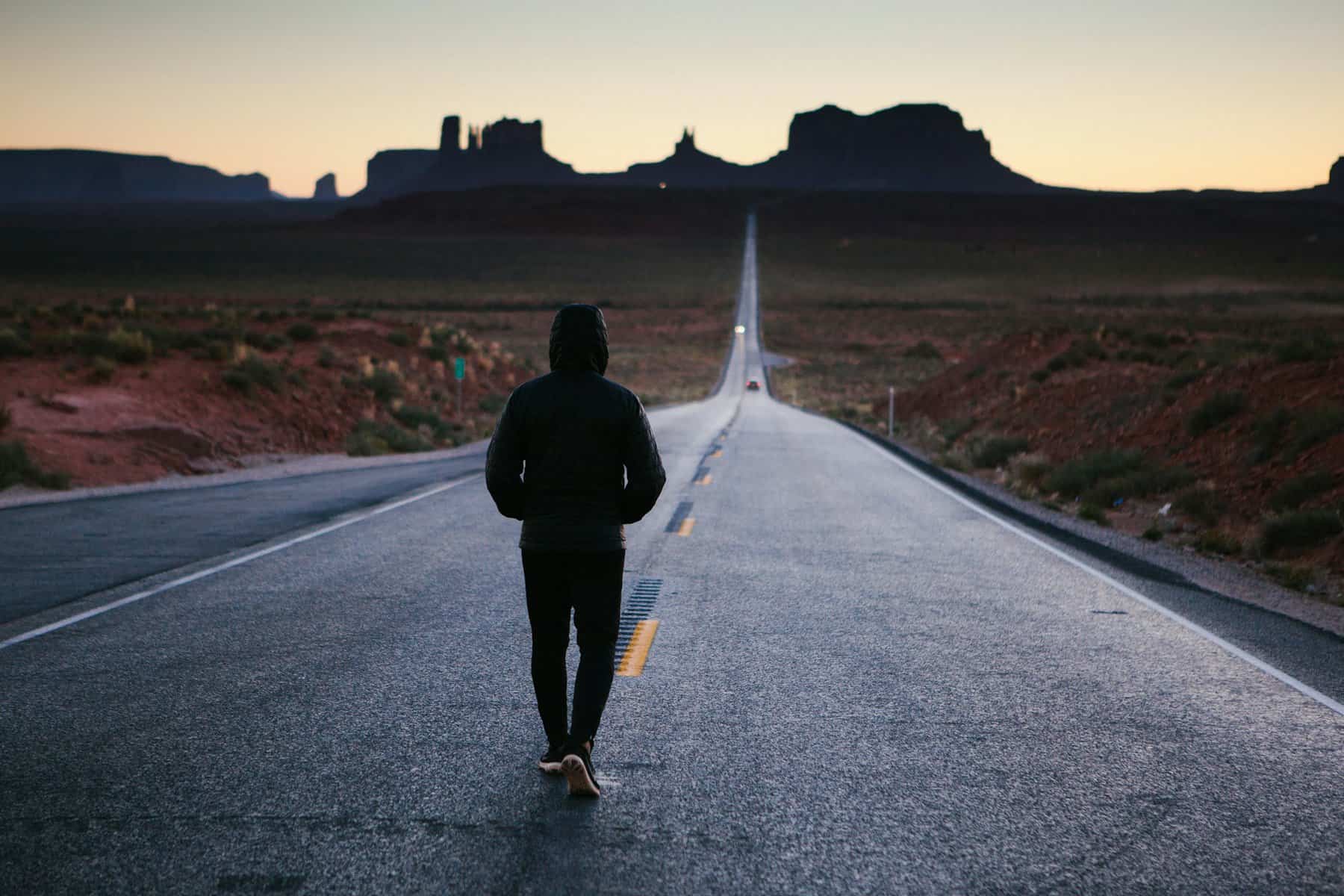 Male teen seen walking away from the camera a desert road.