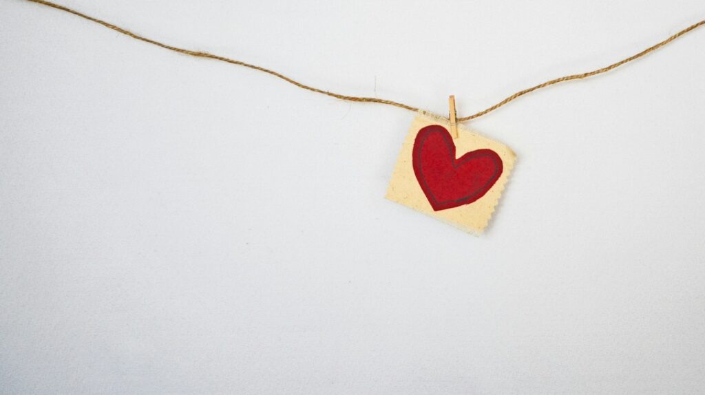 A red heart printed on fabric hangs via clothespin on a twine line.