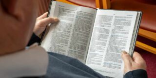 An older person holding a Bible open to the book of Matthew.