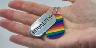 An open hand holds dog tags- one a rainbow, the other say' equality.