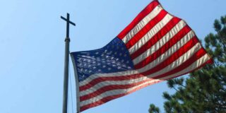 An American flag hangs on a flagpole with a cross on top of it.