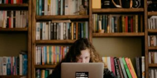 A girl sits behind and is half obscured by a desk and laptop.