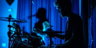 A man sits at a drum set in very low light.