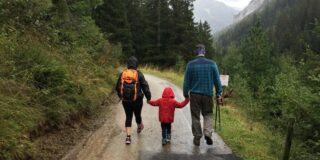 Two adults and a child walk away from a camera on a wet day on an apparent hike.