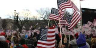 A crowd of people wave small American flags, seen close up.