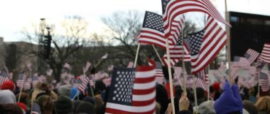 A crowd of people wave small American flags, seen close up.