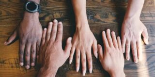 Five hands from men and woman shown flat on a table.