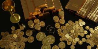 Gold coins, bars, rings and a chalice sit on a table top.