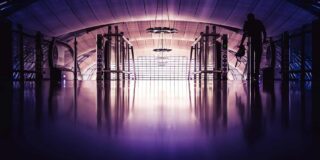 Moody photo of a man in an airport about to go down an escalator.