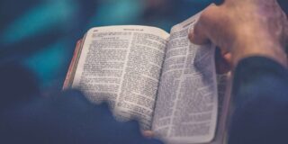 An open Bible sits on a man's lap as he begins to turn a page.